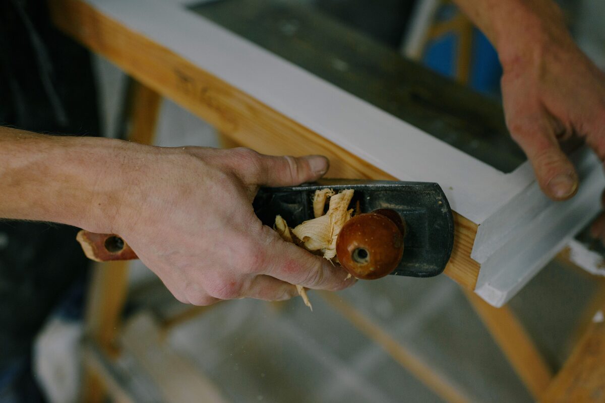 Close-up of hands using a hand plane on white trim and a window frame